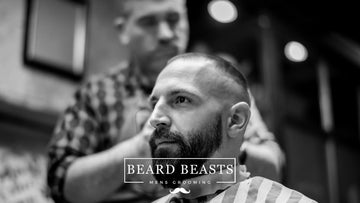 A black and white photo capturing a moment at a barbershop where a man with a beard is receiving a precise 3mm haircut. 
