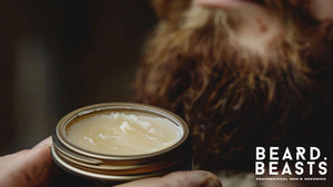 Close-up of a tin of mustache wax, highlighting its texture, with a blurred background featuring a beard—perfect for comparing mustache wax vs beard balm.