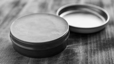 Open tin of natural beard balm on wooden surface with Beard & Beasts logo, featured image for article on Beard Balm vs Beard Conditioner