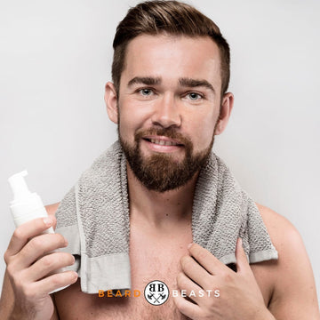Smiling man with a well-groomed beard holding a pump bottle of beard conditioner, featuring Beard Beasts logo, for the featured article on DIY Beard Conditioner.