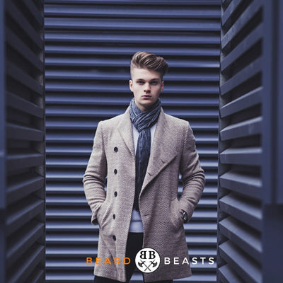 Fashionable young man with styled hair wearing a coat and scarf, representing Beard Beasts' feature article on How To Grow Your Hair Out For Men.