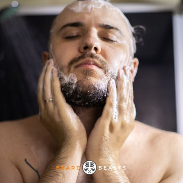 A man with closed eyes, enjoying the sensation of washing his beard with conditioner, featured on the article 