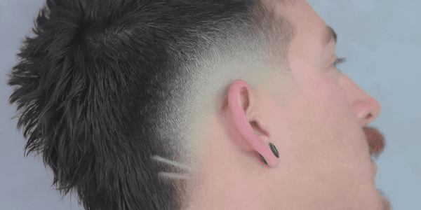 Side profile of a man with a Mohawk Fade hairstyle featuring a high fade and a textured Mohawk. The fade is sharp and clean, with a unique shaved line design near the nape of the neck. 