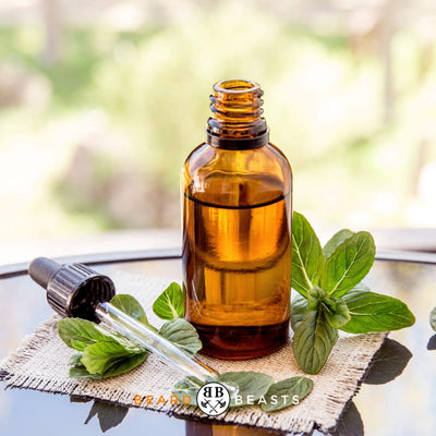 Amber bottle with peppermint oil and fresh peppermint leaves on a burlap cloth - Essential Oils for Men's Grooming - Featured on Beard Beasts' Article on Peppermint Oil for Beard Growth