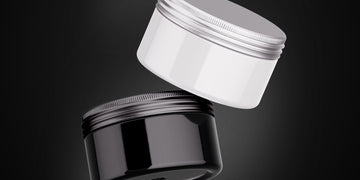 Close-up image of open tins of hair styling products, featuring pomade, wax, and clay on a wooden surface. Highlights the differences in texture and appearance between pomade vs wax vs clay.