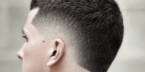 Side profile of a man with a stylish burst fade haircut. The hairstyle features a sharp, clean fade that gradually tapers down the sides and back, creating a rounded "burst" effect around the ears.