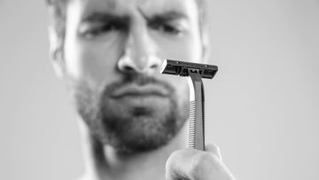 A man skeptically examining a razor blade, possibly contemplating the risk of razor bumps from shaving