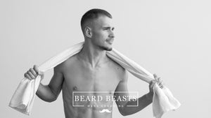Shirtless man with a towel around his neck, looking confident after a grooming session, showcasing the benefits of manscaping.
