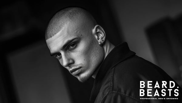 Black and white close-up of a confident young man with a bald fade buzz cut, styled with precision, showcasing sharp facial features and edgy fashion.