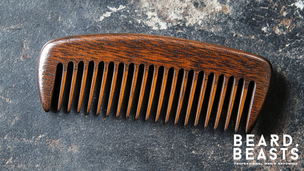 A sandalwood wooden beard comb placed on a textured surface, with the Beard Beasts logo in the corner. Perfect for learning how to comb your beard effectively.