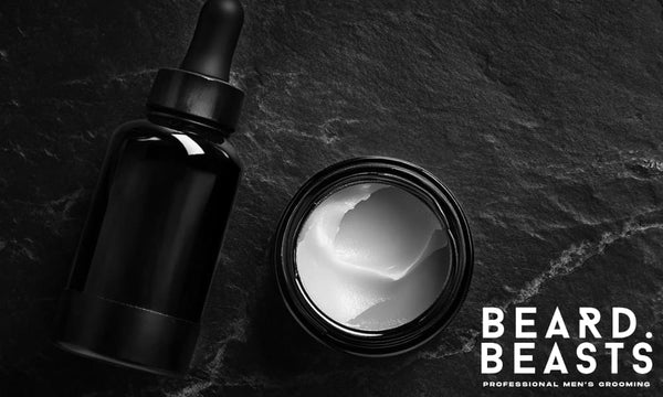 Beard butter in open jar next to dark glass beard oil bottle on black stone background – beard butter vs beard oil comparison