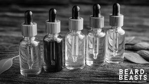 Set of premium glass dropper bottles filled with different natural carrier oils for beard care, displayed on a rustic wooden table.