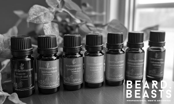 Seven bottles of essential oils for beard growth displayed on a wooden surface with greenery—featuring oils like peppermint, rosemary, and cedarwood.