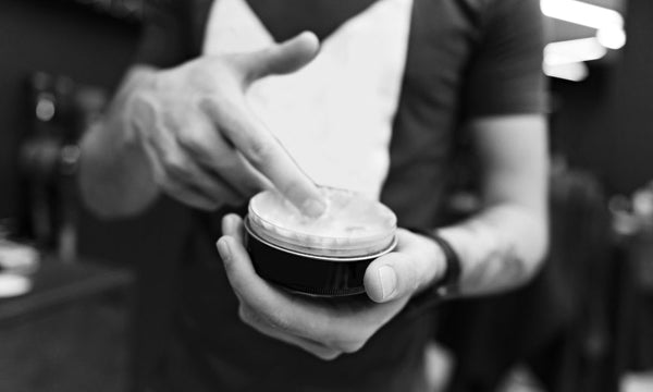 Man applying hair styling clay in a barbershop, showcasing best men’s hair products in use