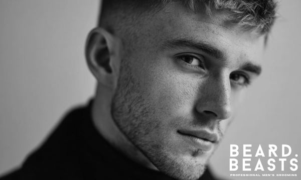 Close-up black and white portrait of a man with sharp, symmetrical stubble and a clean neckline, showcasing a refined designer stubble style.