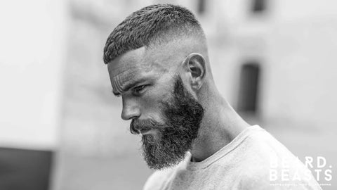 Side profile of a man with a full thick beard and sharp drop fade haircut, a modern grooming look that suits a heart-shaped face