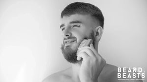 Man exfoliating his beard with a stiff-bristled brush, showing how to exfoliate your beard for healthier growth and grooming.