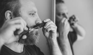 Man trimming his mustache with scissors and a comb in front of a mirror, showing how to trim your mustache with precision.
