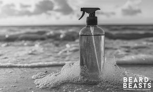 Blue sea salt spray bottle on the beach at sunset, representing how to use sea salt spray for men to achieve natural texture and volume.
