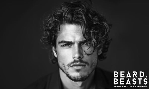 Black and white portrait of a man with voluminous long curly hair styled in loose waves, showcasing a bold and textured long curly hairstyle for men.