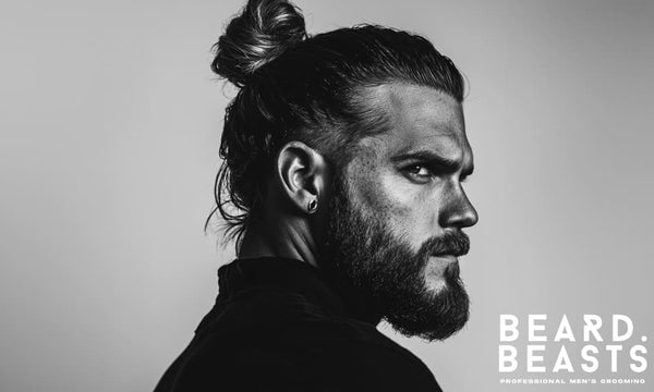 Black and white portrait of a man with a high man bun and full beard, showcasing a bold and modern take on man bun hairstyles.
