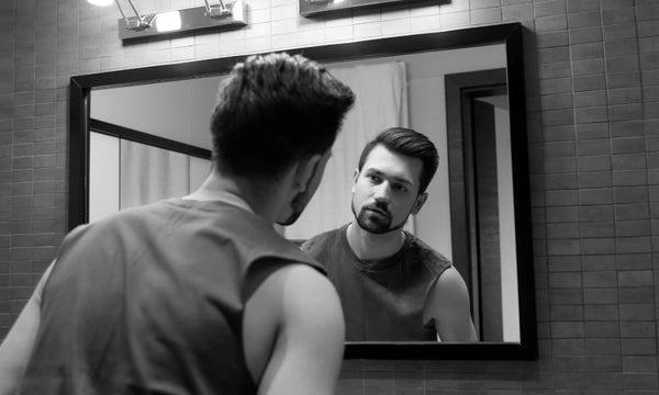 Man looking at his beard in the bathroom mirror, inspecting facial hair for signs of beard shedding or thinning.
