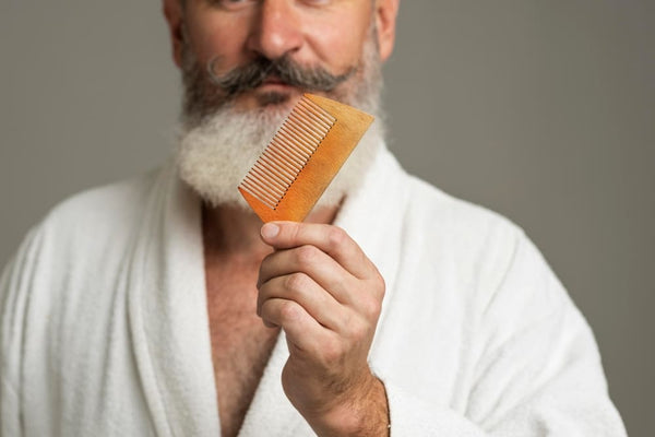 A mature man with a white beard and mustache holding a wooden beard comb, emphasizing proper beard care and how to clean a beard comb for longevity and hygiene.
