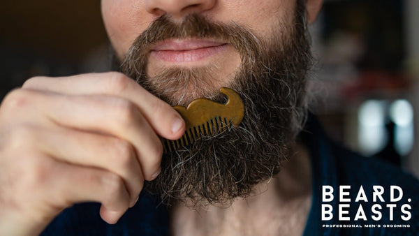 A bearded man gently combing his beard with a small, mustache-shaped metal comb. The act of grooming highlights the importance of daily beard care for maintaining a neat, tangle-free, and healthy appearance. 