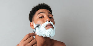 Man with shaving cream on his face using a cartridge razor, contemplating the choice between safety razors vs cartridge razors, highlighting the ease and convenience of modern cartridge razors.