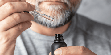 A man is applying beard oil using a dropper, carefully measuring the amount—a step in determining how often you should apply beard oil for effective beard care.