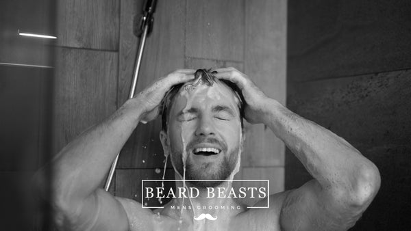 A man joyfully washing his hair in the shower, illustrating a routine for male grooming and hair care with an emphasis on determining how often should men wash their hair.
