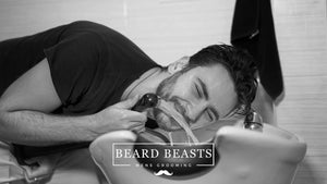 Smiling man leaning over sink using premium beard wash, highlighting the grooming choice of beard wash vs shampoo for men.