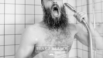A man with a long beard joyfully rinsing it under the shower, showcasing the process of how to wash your beard.