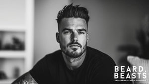 Black and white portrait of a man with a stylish skin fade pompadour and a well-groomed beard, exuding confidence and sophistication. 
