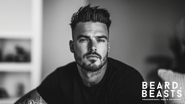 Black and white portrait of a man with a stylish skin fade pompadour and a well-groomed beard, exuding confidence and sophistication. 