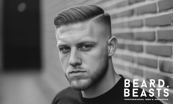 portrait of a young man with a high drop fade comb-over and a sharp side part, posing against a brick wall. 