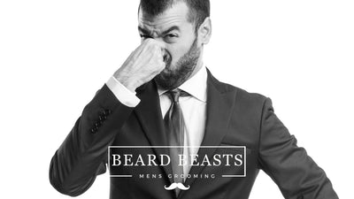 A monochrome image of a well-dressed man in a suit holding his nose and making a disgusted expression, suggesting a smelly beard