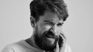 Man grimacing in pain touching his beard due to ingrown beard hairs.