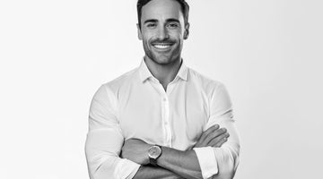 Confident man sporting stubble in a white shirt with crossed arms, embodying the modern debate of clean shaven vs stubble styles in men's grooming.