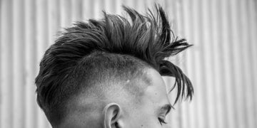 Close-up of a stylish men's haircut featuring a textured faux hawk with short sides. The hair is spiked and voluminous on top, showcasing modern men's hair care and grooming techniques. 