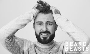 Frustrated bearded man pulling his hair, showing the impact of common men’s hair styling mistakes.