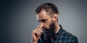 Man with a stylish slicked back haircut and a full beard, wearing a plaid shirt, looking thoughtful. Ideal example of a modern, sophisticated slicked back hairstyle.