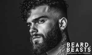 Close-up black and white portrait of a man with a thick curly beard, tight fade haircut, and confident expression—ideal look for curly beard grooming.