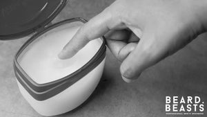 Close-up of a hand dipping into Vaseline petroleum jelly, often considered for beard use but not recommended for facial hair care.